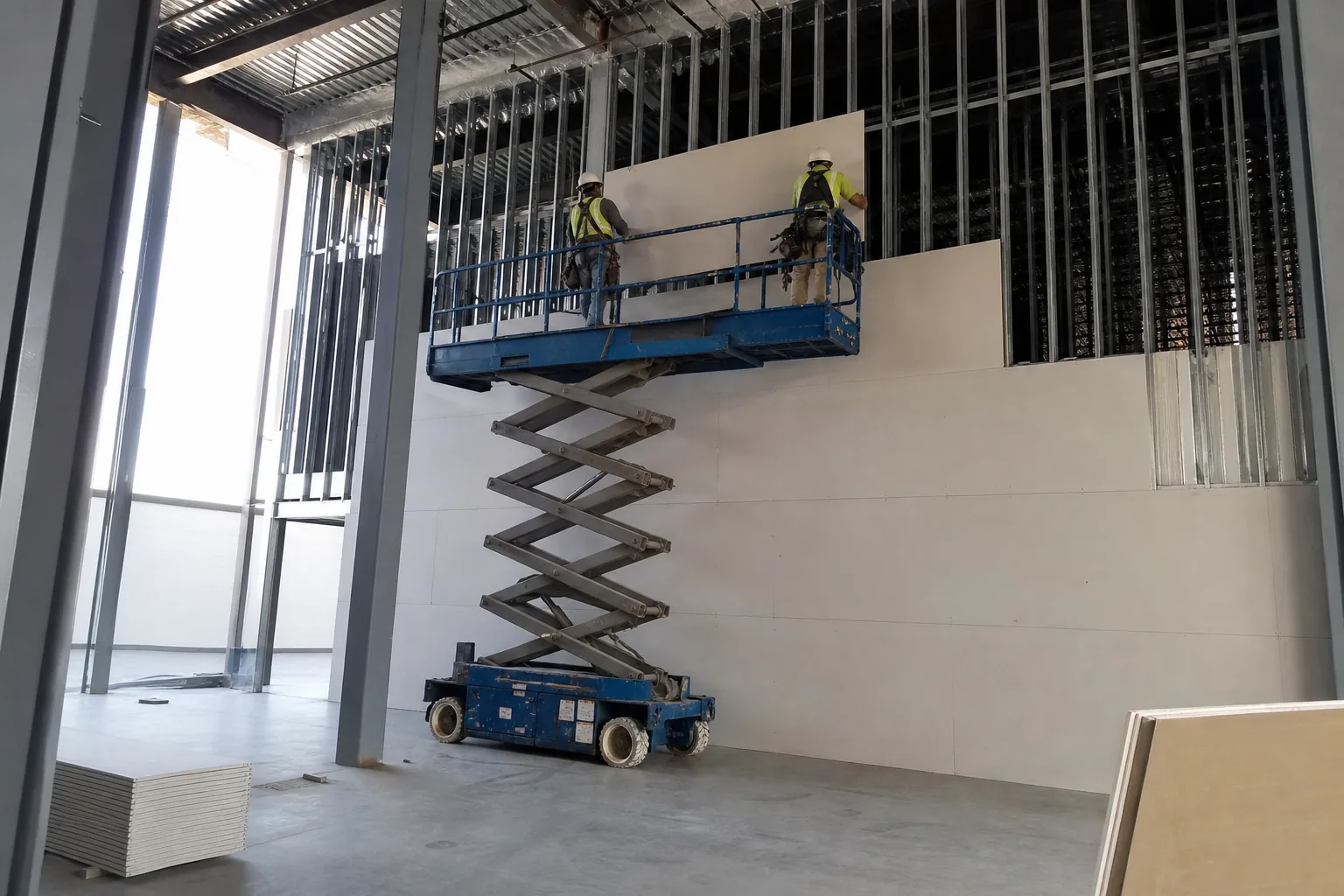 Crew on a scissor lift hanging drywall on a tall commercial wall in Noblesville, IN