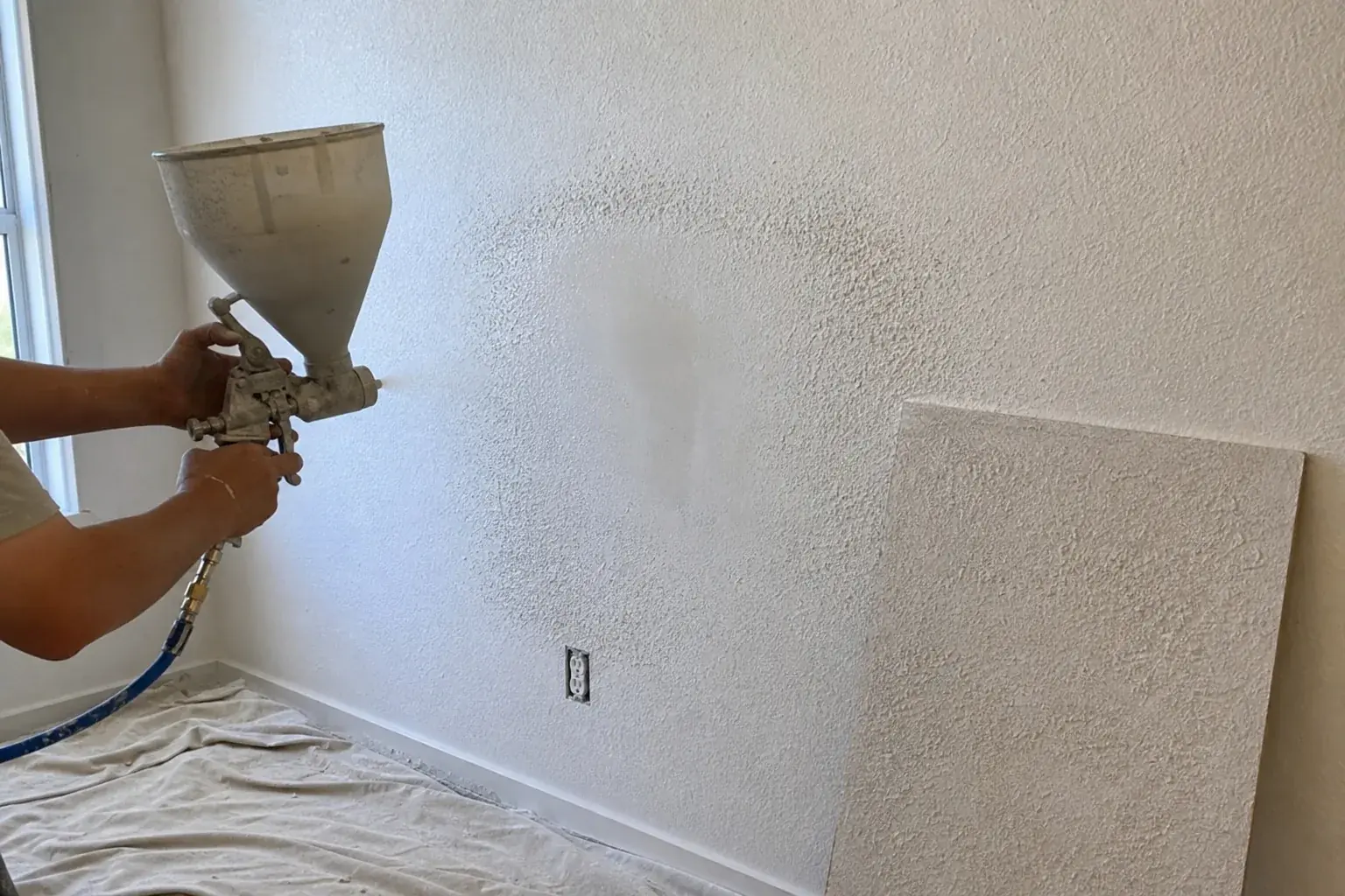 Hopper gun spraying knockdown texture to blend a drywall repair in Noblesville, IN