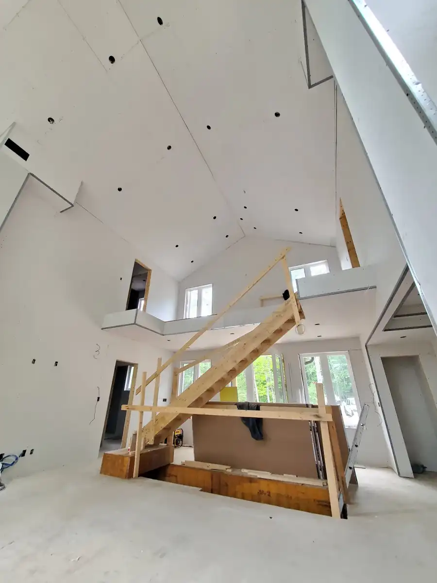 Two-story great room in a custom home with drywall hung and taped, tall windows and a vaulted ceiling