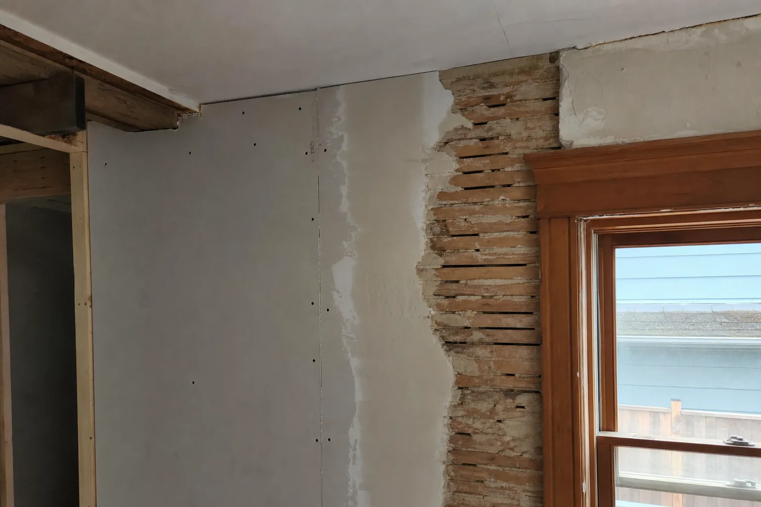 New drywall tied into original plaster and lath beside a wood window casing in an older Meridian Hills home
