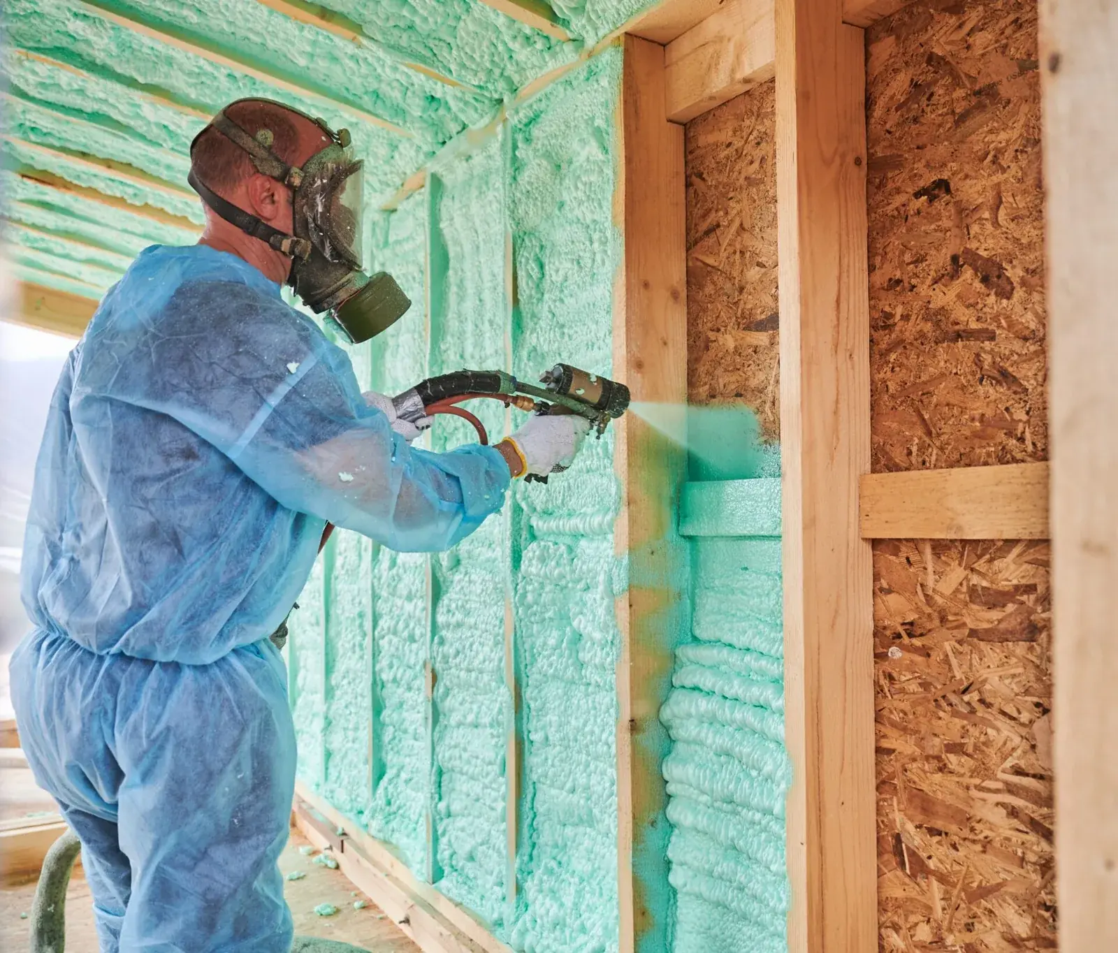 Installer in protective gear spraying closed cell foam insulation between wall studs in a Noblesville, IN home